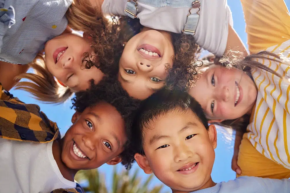 Fröhliche Kinder stecken im Kreis die Köpfe zusammen