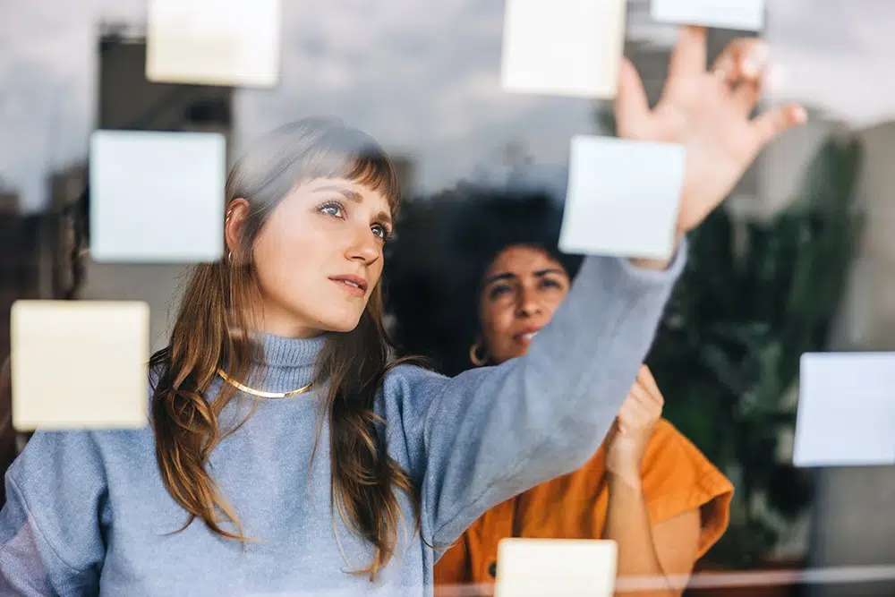 idee-on-vernetzung-postits-ideen-finden Frau sammelt Ideen mit Notizzetteln an einer Glaswand